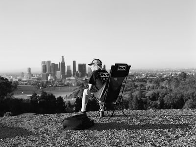 a man taking in city views lounging in a black camp chair on a grassy hill. a man taking in city views lounging in a black camp chair on a grassy hill.