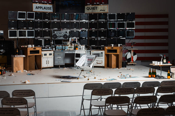 A stage setup with rows of chairs facing a wall of television monitors.