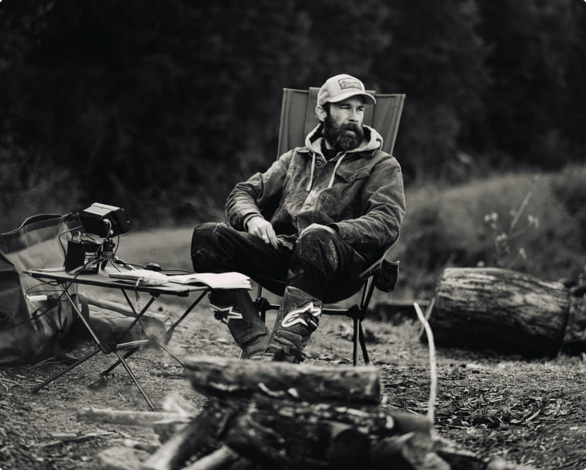 A bearded man sitting in a Helinox high-back camp chair by a campfire