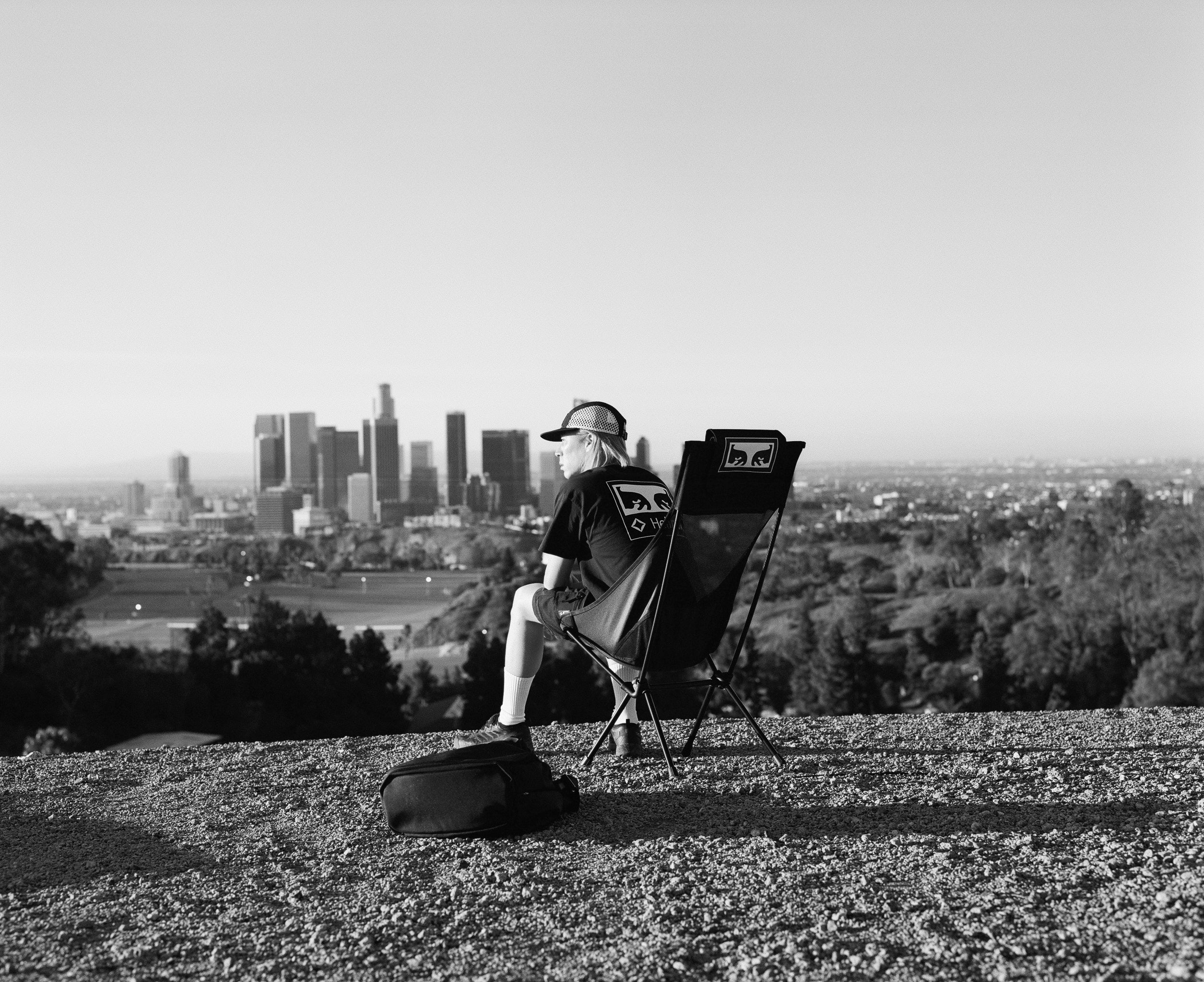a man taking in city views lounging in a black camp chair on a grassy hill.