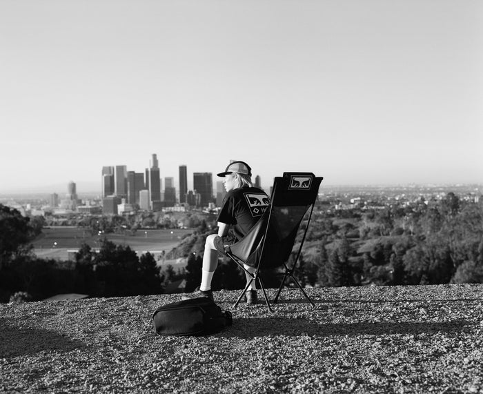a man taking in city views lounging in a black camp chair on a grassy hill.