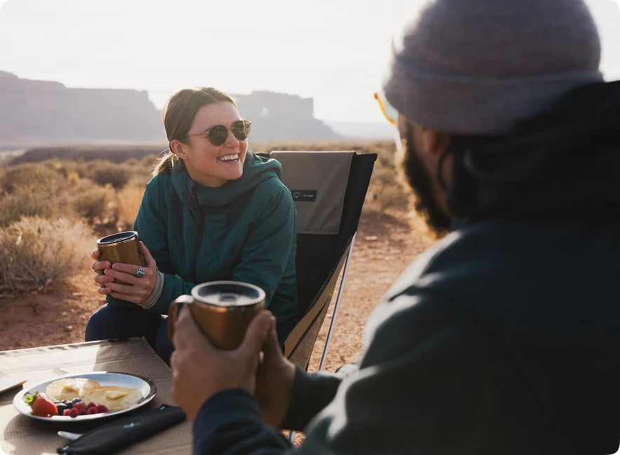 Friends sharing coffee in Helinox chairs at a desert campsite