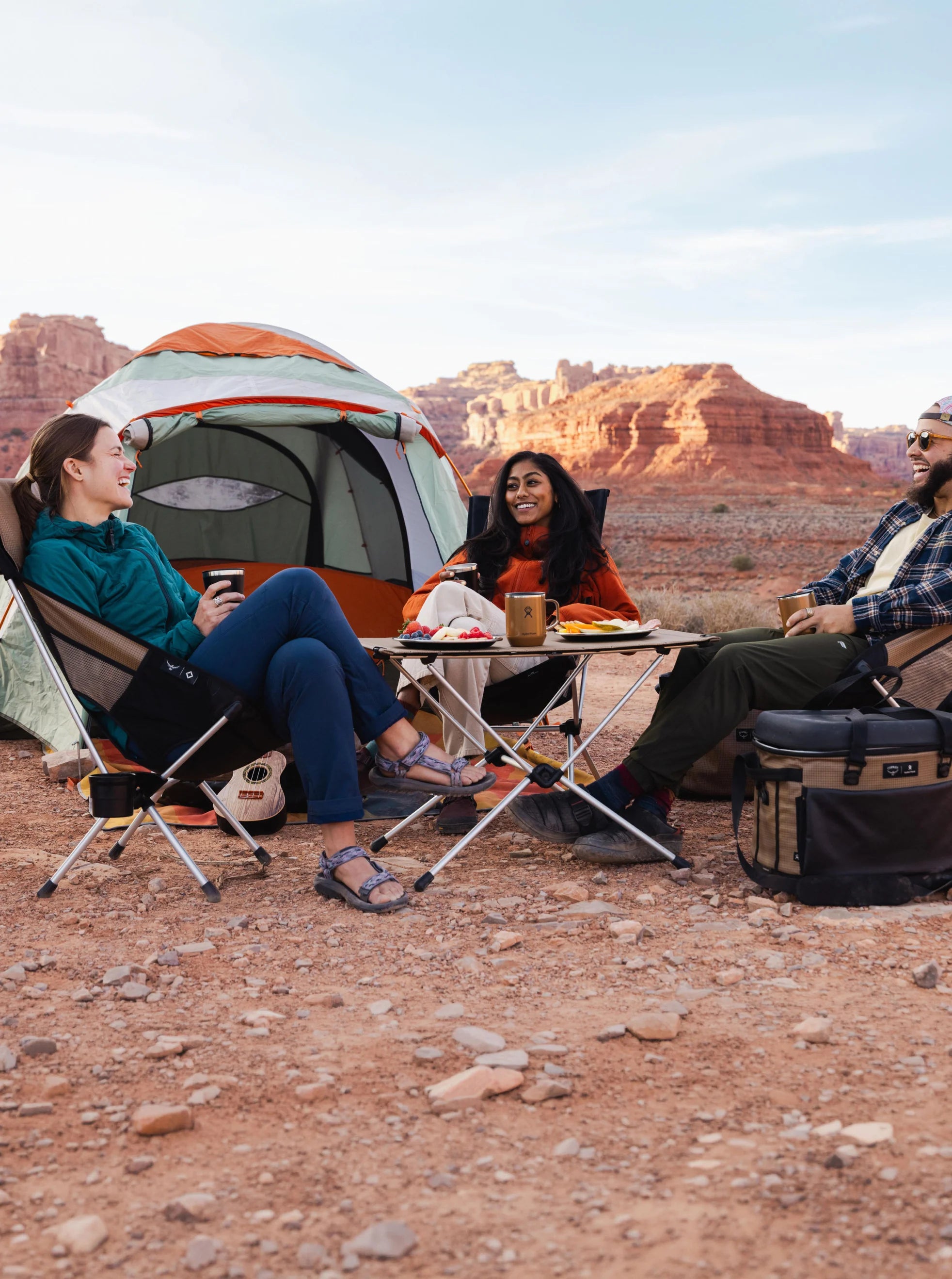 Three friends relaxing in Helinox chairs by a tent at dusk
